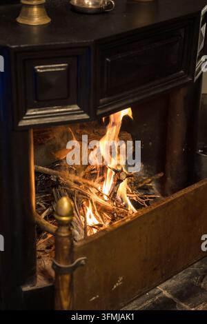 Rustikaler Holzofen mit glühenden Flammen und Brennholz in einem gemütlichen Wohninterieur Stockfoto