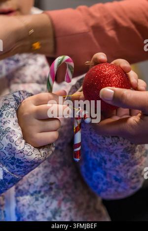 Elternteil und Kind schmücken den Weihnachtsbaum mit Zuckerstangen und Ornamenten Stockfoto