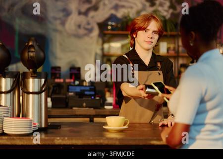 Barista nimmt kontaktloses Mobiltelefon-Zahlung von einer schwarzen Frau im Café entgegen Stockfoto