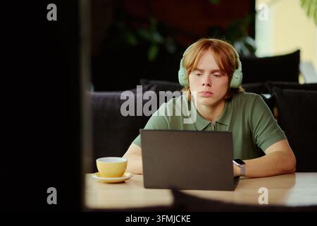 Junger Mann mit Kopfhörern, der im Café online am Laptop lernt Stockfoto