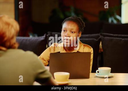 Schwarze Frau spricht mit einem Kollegen während eines Geschäftstreffens im Café Stockfoto