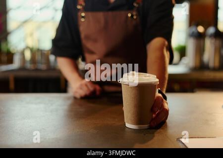 Männlicher Barista serviert Pappkaffeebecher zum Mitnehmen an der Café-Theke Stockfoto