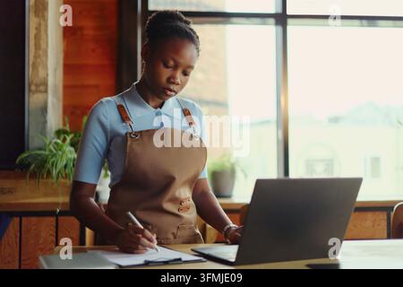 Schwarze Frau als Kleinunternehmerin verwaltet Bestellungen auf einem Laptop Stockfoto