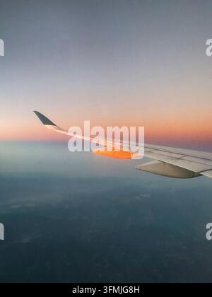 Flügel eines Flugzeugs über Wolken bei einem farbenfrohen Sonnenaufgang Stockfoto