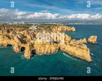 Luftaufnahme von Ponta da Piedade in Lagos, Algarve, Portugal, mit Klippen, Meeressäulen und der Stadt am Horizont unter einer bewölkten Himmel. Stockfoto