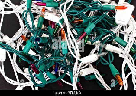 Nahaufnahme von chaotischen festlichen elektrischen Kabeln mit mehrfarbigen Glühbirnen, die darauf warten, für die Weihnachtsdekoration entwirrt zu werden. Stockfoto