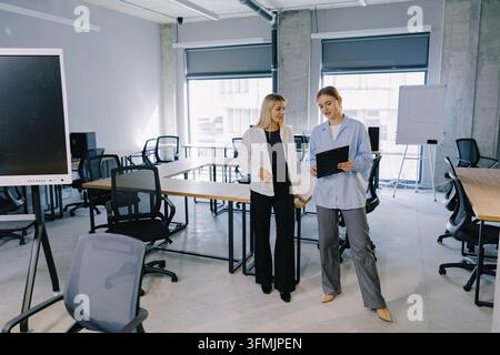 Zwei junge Geschäftsfrauen, die Dokumente besprechen und in einem modernen Bürositzungssaal zusammenarbeiten, wobei sie sich auf Teamarbeit konzentrieren Stockfoto