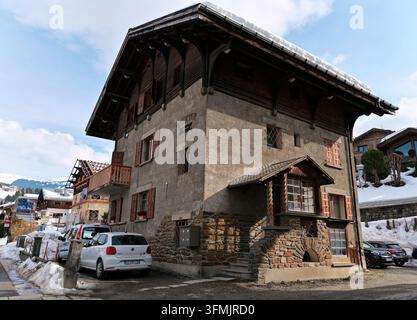 Altes Chalet aus Stein und Holz mit geschnitzten Dachvorsprüngen und einem schneebedeckten Dach in einer ruhigen Straße in Megève Stockfoto