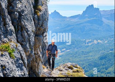 Männlicher Bergsteiger geht entlang eines freiliegenden Felsvorsprungs nach der via ferrata-Besteigung in den Dolomiten, Italien. Das alpine Tal und die dramatischen Gipfel betonen Ausdauer, Höhe und Outdoor-Abenteuer Stockfoto