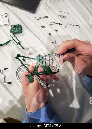 Ein Mann, der eine winzige Schraube in einem Miniatur-Metallbausatz festzieht, Nahaufnahme von männlichen Händen, die das Modell mit einem Schraubenzieher zusammenbauen Stockfoto