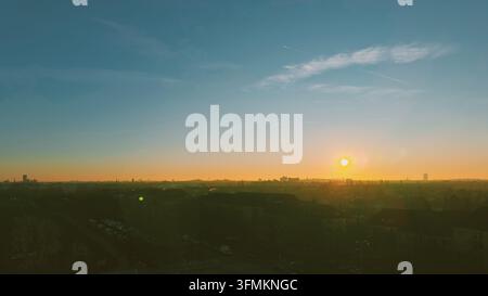 Weite atmosphärische Aussicht über eine Vorstadtlandschaft in Richtung einer fernen Stadt Skyline, beleuchtet vom warmen Licht der untergehenden Sonne. Stockfoto