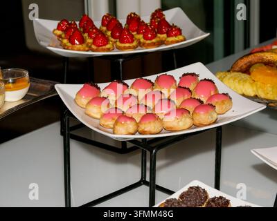 Verschiedene kleine Desserts, die auf gestuften weißen Tellern bei einer Indoor-Veranstaltung präsentiert werden. Stockfoto