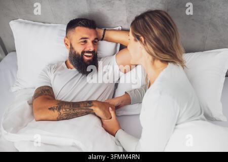 Das junge, glückliche Liebespaar liegt morgens im Bett. Sie sind entspannend und lächeln. Stockfoto