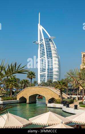 Ikoniches Hotel Burj Al Arab in Segelform, das über einer steinernen Bogenbrücke und Wasserwegen im Madinat Jumeirah Souk Resort, Dubai, Vereinigte Arabische Emirate aufragt Stockfoto