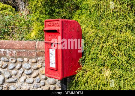 Traditioneller roter britischer Briefkasten, der an einer Steinmauer in einem ländlichen Dorf in Großbritannien montiert ist Stockfoto