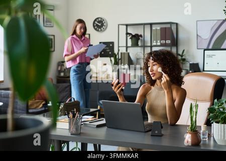 Bimorphe Frau, die Make-up an einem Schreibtisch in einem modernen Kreativstudio auftragt Stockfoto