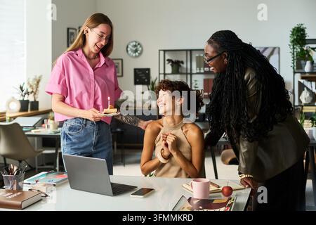 Verschiedene Kollegen feiern den Geburtstag einer biracialen Frau in einem modernen Büro Stockfoto