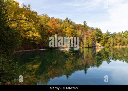 Pink Lake im Gatineau Park, Quebec, Kanada. Malerische Uferlinie mit lebhaftem Herbstlaub. Herbstlandschaft aus Wald, der ruhiges Wasser unter blauem Himmel umgibt Stockfoto