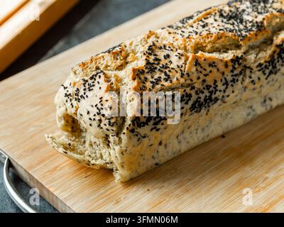 Rustikales hausgemachtes Brot mit einer knusprigen goldenen Kruste und reichlich schwarzen Samen auf einem Holzbrett. Stockfoto
