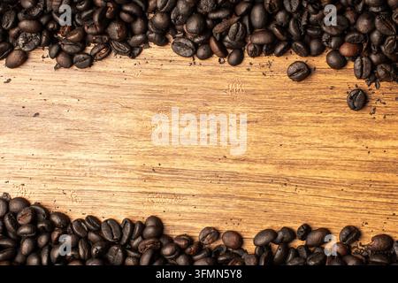 Flächenlayout-Oberansicht von dunkel gerösteten Kaffeebohnen, die horizontalen oberen und unteren Rand auf Holzuntergrund bilden, mit großem Kopierraum in der Mitte. Stockfoto