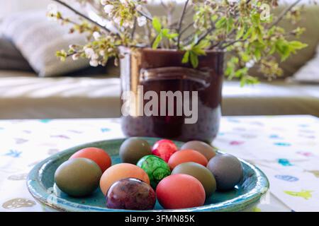 Bunte Ostereier und Vase mit blühenden Zweigen auf Tisch mit Ostertischdecke Stockfoto