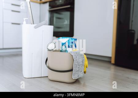 Nahaufnahme eines Eimers mit Mopp, Reinigungsmitteln, Gummihandschuhen und Wut auf dem Boden vor einem unscharfen Hintergrund einer modernen Küche. Reinigungsbegriff, sauber Stockfoto