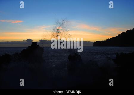 Sonnenaufgang begrüßt den Morgen im Laupahoehoe Beach Park auf der Big Island von Hawaii. Schwarze Kliffs bilden ein Resonanzbrett für die Wellen, während das Licht co Stockfoto