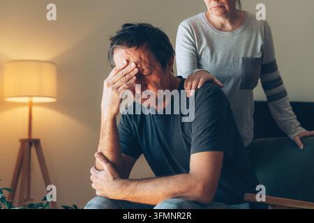 Frau tröstet einen gestressten Mann, indem sie eine Hand auf seine Schulter legt, Unterstützung und Empathie-Konzept, Mann hält seinen Kopf zu Hause, warmes gemütliches Interieur. Sele Stockfoto