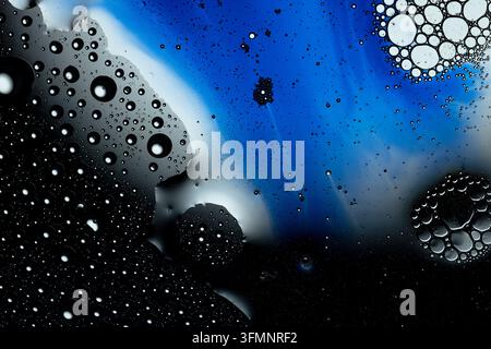 Abstrakter Kunsthintergrund mit Öl und Wasser, die sich trennen und verschiedene Blasen und flüssige Muster in blauen und schwarzen Farben bilden Stockfoto