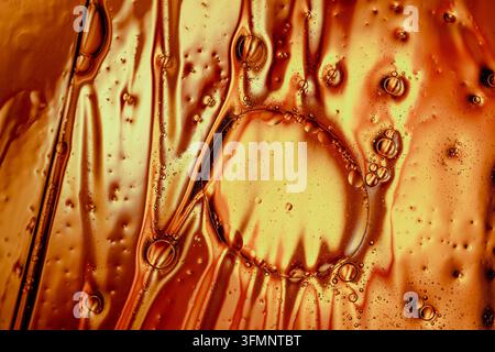 Abstrakte Textur, die sich mit goldenen Öltropfen und Luftblasen bildet, die sich in einer zähflüssigen Flüssigkeit vermischen und die Fluiddynamik zeigen Stockfoto