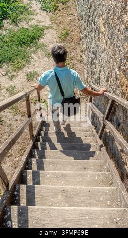 Hochwinkelaufnahme eines männlichen Touristen, der eine Holztreppe entlang der alten Mauer der Akkerman-Festung in Bilhorod-Dnistrovskyj, Ukraine, hinuntergeht. Sommerrundfahrt Stockfoto