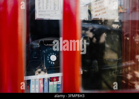 Nahaufnahme eines Vintage-schwarzen Wählscheibentelefons in einer ikonischen roten Telefonzelle Stockfoto