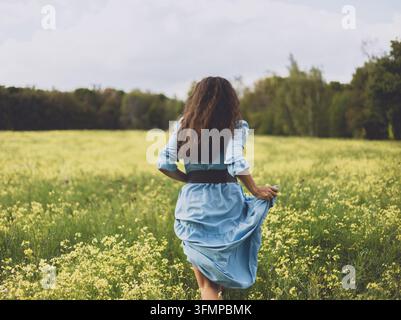 Junge Frau rennt durch eine Wildblumenwiese in einem blauen Kleid Stockfoto