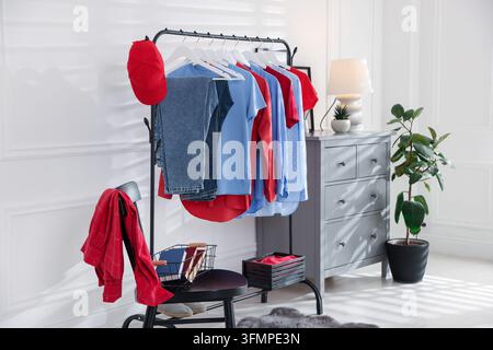 Verschiedene Kleidungsstücke hängen an einem Kleiderständer, Baseballkappe und Dekoration im Innenraum Stockfoto
