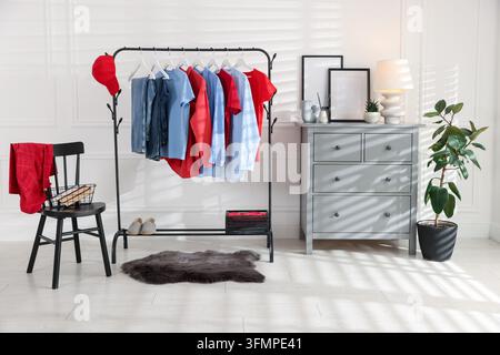 Verschiedene Kleider hängen an einem Kleiderständer, Baseballkappe, Schuhe und Dekoration im Innenraum Stockfoto
