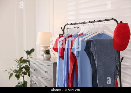 Verschiedene Kleidungsstücke und Baseballkappe hängen an einem Regal im Innenraum, Nahaufnahme. Platz für Text Stockfoto