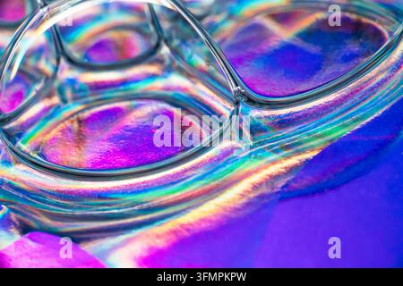 Makroabstrakt überlappender Glaslinsen, die lebendige irisierende Regenbogenreflexionen über eine leuchtende blaue, violette, rosa und türkisfarbene Oberfläche erzeugen Stockfoto