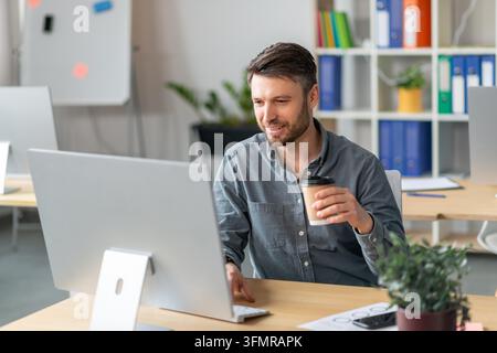 Junger Mann arbeitet am Computer mit Kaffee im Büro, Geschäftskonzept Stockfoto