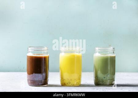 Vielzahl von bunten Iced Latte Getränke. Eiskaffee, Kurkuma und Matcha Latte Cocktails in Gläsern über Grau Grün Textur Hintergrund. Platz kopieren Stockfoto