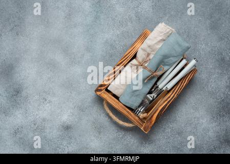 Besteck und LeinenServietten in einem Holztablett. Grauer Grunge-Betonhintergrund. Ansicht von oben. Stockfoto