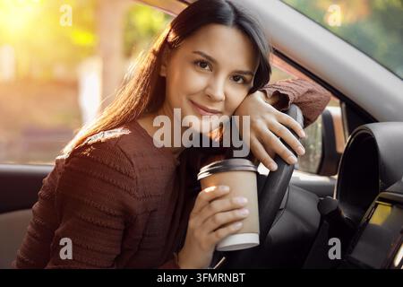 Pendler-Lebensstil und Morgenroutine, glückliche Frau hält eine Kaffeetasse, während sie während des Sonnenaufgangs im Auto sitzt, für die tägliche Reise und urbane Mobilität Stockfoto