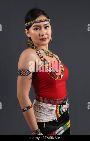 Seitenansicht-Porträt einer ernsten jungen Sabahanerin in traditioneller Murut Tahol Simba-Tracht vor Studiohintergrund. Stockfoto