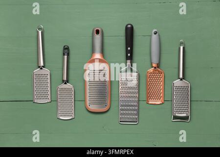 Kochen und Nahrungszubereitung, Sammlung verschiedener metallischer Küchenreibe für Käse und Gemüse, angeordnet auf einer rustikalen grünen Holzoberfläche Stockfoto