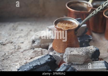 Türkischer Kaffee wird auf offenem Feuer in einem kleinen Metalltopf auf glühenden Kohlen zubereitet Stockfoto