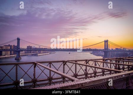 Sonnenaufgang über der Manhattan Bridge von der Brooklyn Bridge aus, New York City, USA, unter bunten Wolken, die über dem East River leuchten. Stockfoto