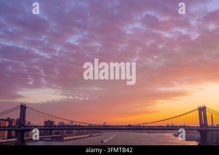 Sonnenaufgang über der Manhattan Bridge von der Brooklyn Bridge aus, New York City, USA, unter bunten Wolken, die über dem East River leuchten. Stockfoto
