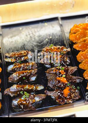 Eine gegrillte Sushi-Rolle und ein glasierter Fischplatte, präsentiert auf einem japanischen Lebensmittelmarkt mit lebhaftem orangefarbenem Belag und garniert mit Meeresfrüchten Stockfoto