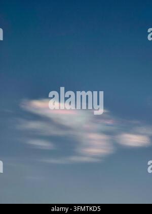 Eine pastellfarbene Wolke zieht über den tiefblauen Himmel und schafft eine weiche atmosphärische Szene mit verschwommenen Rändern, subtilen rosa Highlights und ruhiger natürlicher Schönheit Stockfoto