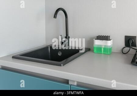 Detaillierter Blick auf einen modernen Spülbereich mit eleganten schwarzen Armaturen, grauer Rückwandverkleidung und Geschirrspül-Zubehör unter hellem Indo Stockfoto