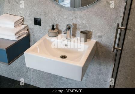 Detaillierter Blick auf einen zeitgenössischen Badezimmerwaschbereich mit stilvollen Keramikarmaturen, Wandfliesen mit Steintextur und Hygieneprodukten, Wohnraumdekoration Stockfoto